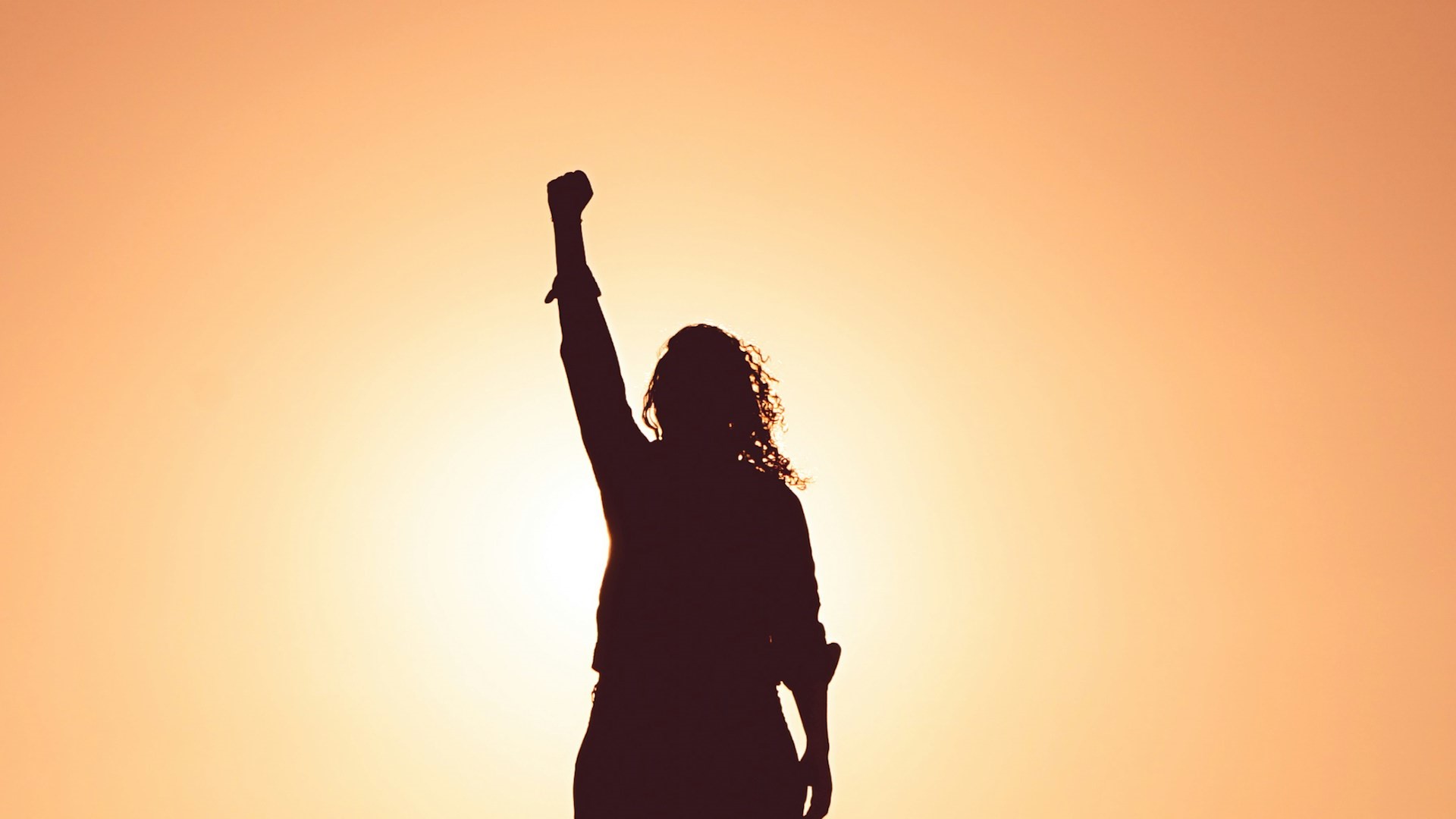 Silhouet van persoon met opgeheven vuist tegen een oranje zonsondergang, symbool voor vitaliteit op de werkvloer