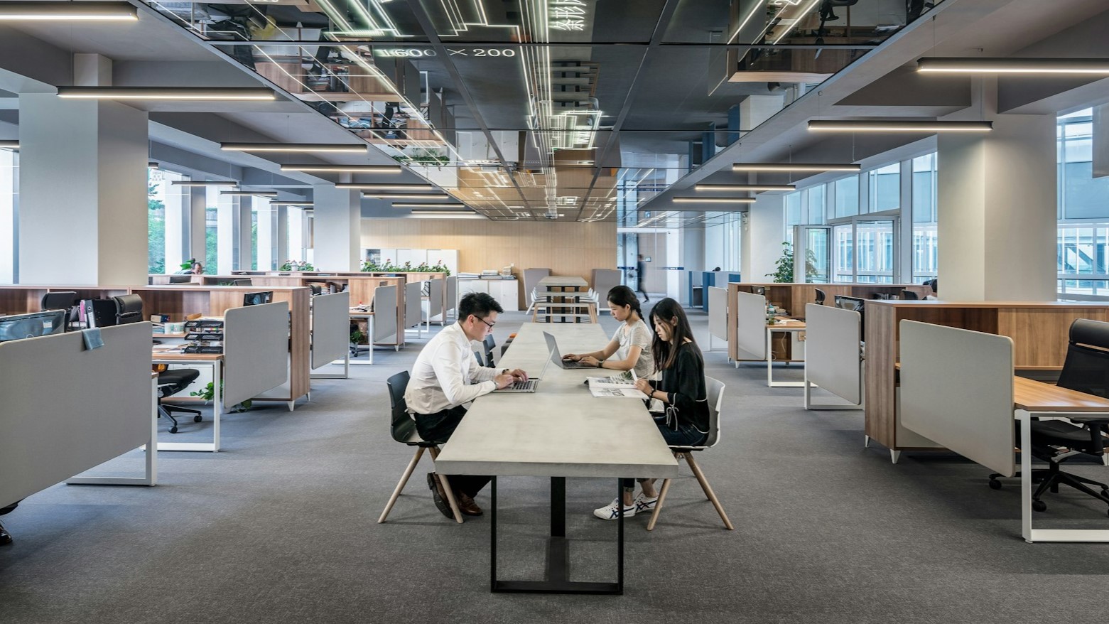 Moderne kantoorruimte met drie collega’s die samenwerken aan een lange tafel, passend bij een cadeau voor collega’s